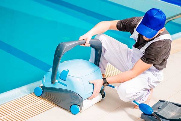 Pool service technician working hands-on with a robotic pool cleaner at poolside — the daily route reality EZ Pool Biller is built around